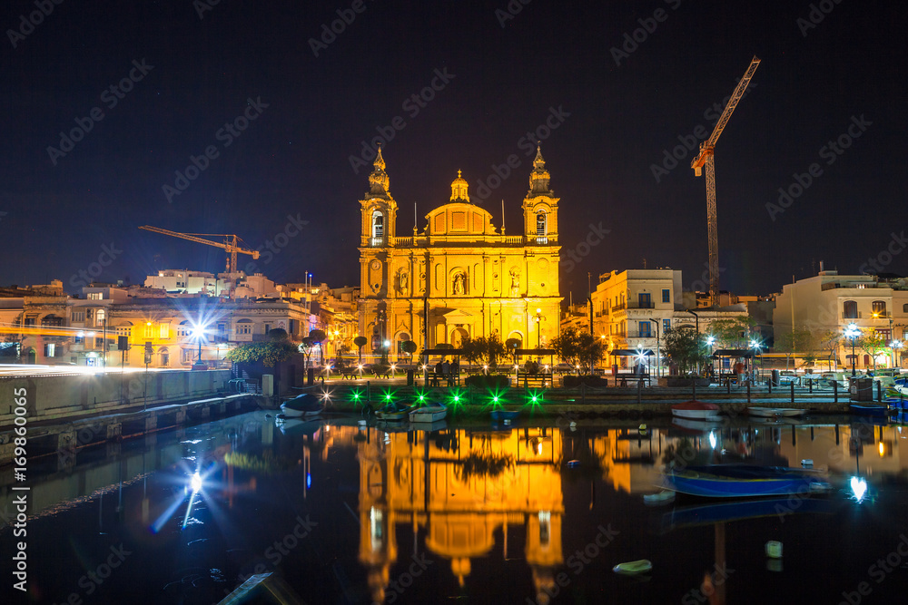 The beautiful Msida Parish Church at deep night with harbor at the foreground. Malta.
