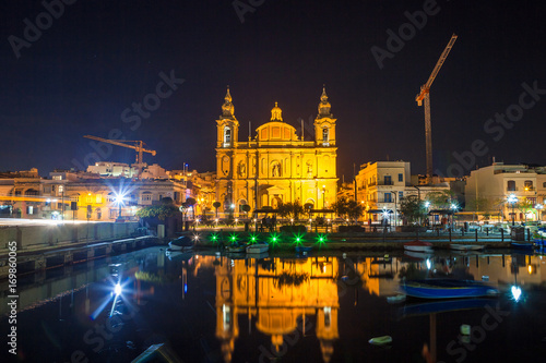 The beautiful Msida Parish Church at deep night with harbor at the foreground. Malta.