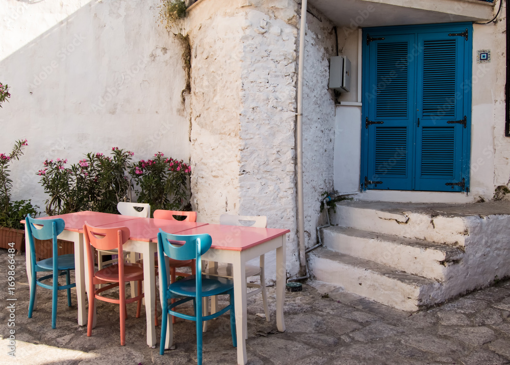 Old streets and houses of Marmaris. Table with colorful chairs (blue, pink, white) stands near entrance to the house with blue east Oriental input doors in old town of the resort of Marmaris in Turkey