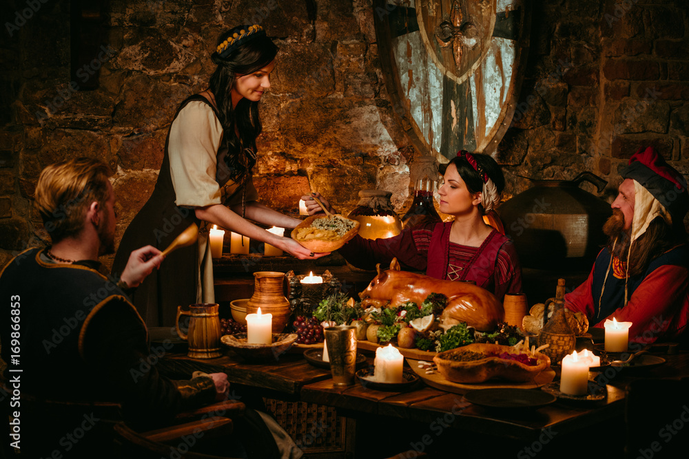 Medieval people eat and drink in castle tavern.