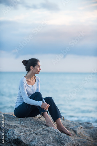 A beautiful young brunette sitting on a rock at the beach