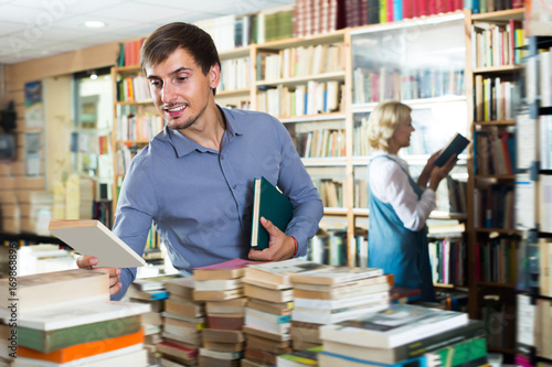 Young laughing man choosing new book from many