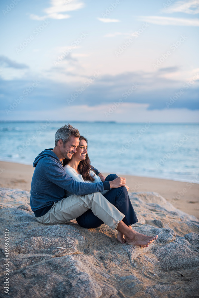 Beautiful couple sitting at the beach watching the sunset