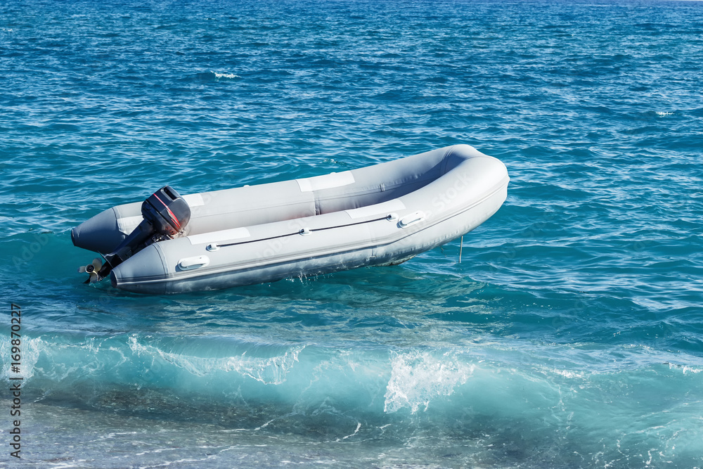 Naklejka premium Inflatable boat with a motor swings on sea waves near the shore