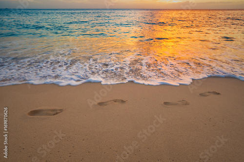 Footprints on beach sand with sea wave with foam at sunset time. Foot steps among waterline tropical vacation design