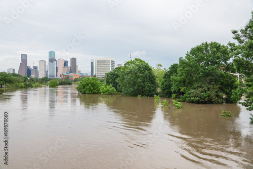 High and fast water rising in Bayou River along Allen Parkway and Memorial Drive with downtown Houston in background under storm cloud sky. Heavy rains from tropical storm caused many flooded areas photo