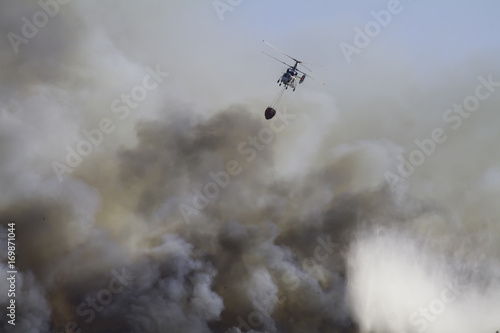 Wild fire close to houses being fought with airplanes and helicopters