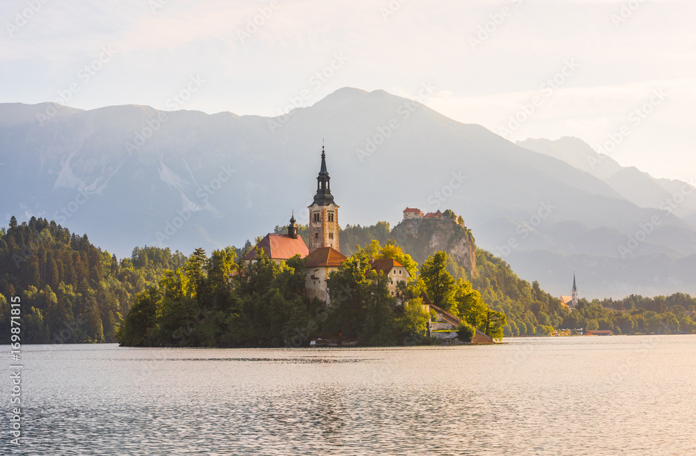 Famous Catholic Church on Little Island in Bled Lake and Bled Castle on a Rock in Slovenia with Mountains in Background at Sunrise