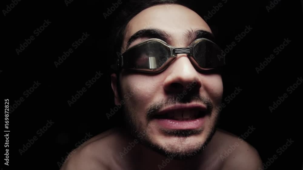 A weird looking man close up wearing googles and making signs with his hands. Pure black background. A weird looking man close up wearing googles and making signs with his hands. Pure black background.