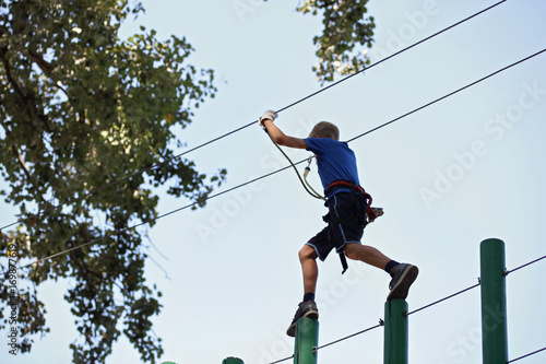 10 years old boy in rope adventure park. Climbing, high wire park, teenager in safety equipment. Challenge, reach the goal, success, breaking fear concept