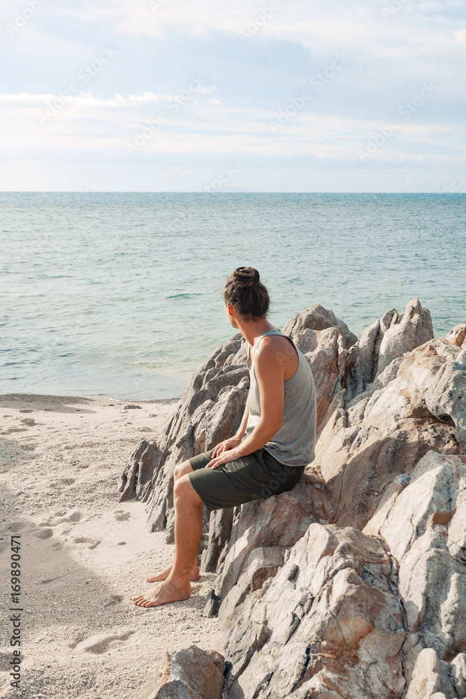 young man sitting on the beach and look on the horizon line