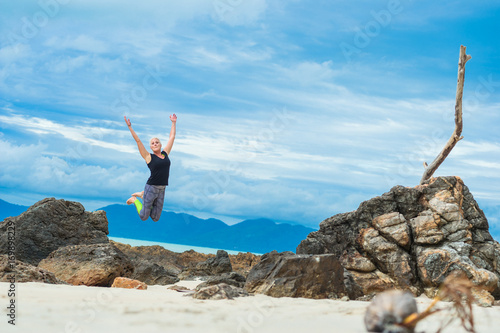 Beautiful mature aged woman jumps and having fun on a desert tropical beach