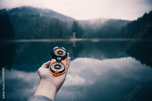 Compass in holding hands on mountain lake background