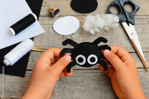 Small girl holds a felt spider ornament in his hand. Girl made a Halloween felt spider crafts. Easy felt crafts for beginners. Halloween sewing craft kit