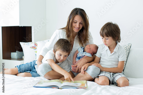 Young mother, read a book to her three children, boys, in the bedroom