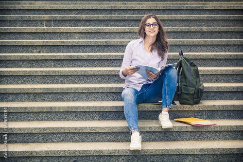 Happy young woman wearing glasses, reading near university. The student. © Oleksandr