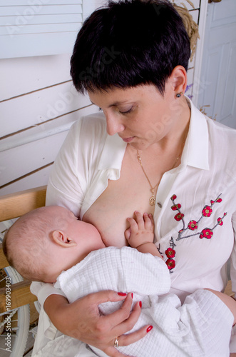 Breastfeeding baby. Young mother holding her newborn child. Mom nursing baby. Woman and new born boy in white bedroom.