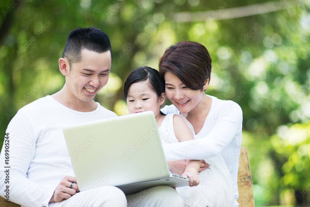 Young happy Asian family looking at the computer together at the park. Young happy Asian family looking at the computer together at the park.