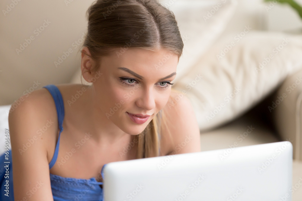 Portrait of beautiful young woman lying on sofa at home and using laptop. Attractive millennial lady browsing online, watching movie on computer, communicating with friends in social network, shopping Portrait of beautiful young woman lying on sofa at home and using laptop. Attractive millennial lady browsing online, watching movie on computer, communicating with friends in social network, shopping