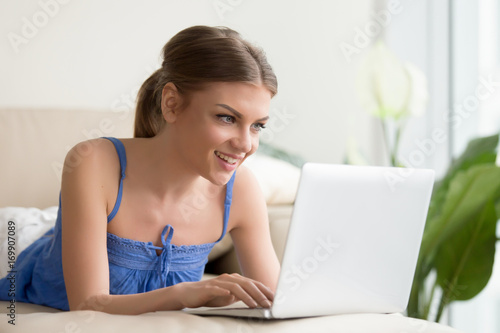 Happy smiling young woman using laptop while resting on sofa at home. Beautiful lady relaxing and having fun with electronic device  playing computer games  chatting with friends online  enjoying app