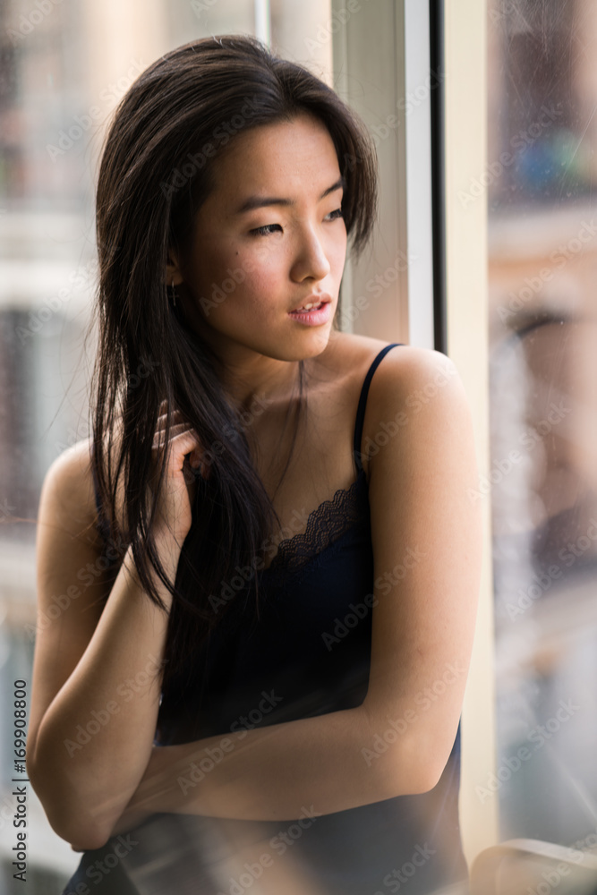 Portrait Of Beautiful Chinese Woman Indoors Next To A Window With Natural Light Stock Photo
