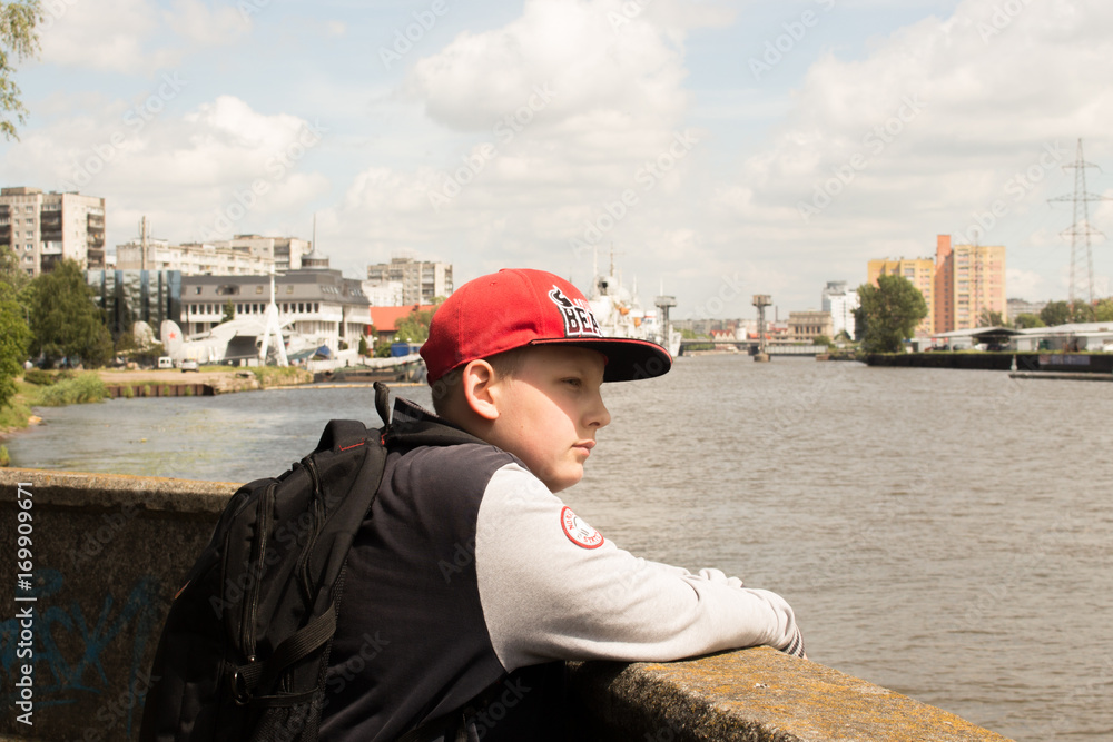 boy in a red cap stands near the river
