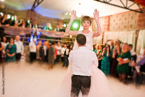 Wedding couple dancing their first wedding dance with heavy smoke and different lights in the restaurant full of guests.