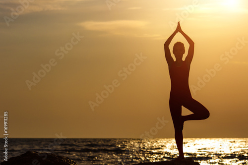 A woman in a red suit practicing yoga on stone at sunrise near the sea