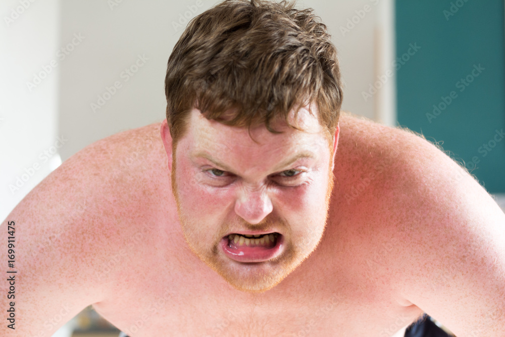 Fototapeta premium Rothaariger junger dicker Mann schreit wütend und zerreißt sein Shirt