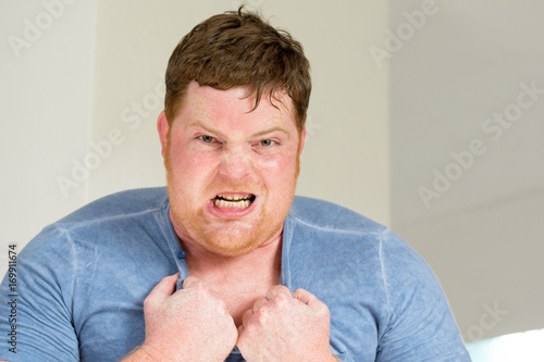 Rothaariger junger dicker Mann schreit wütend und zerreißt sein Shirt