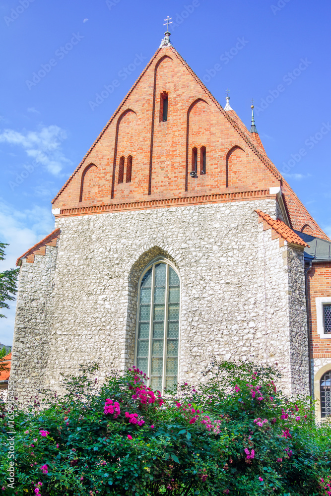 View of old stone Catholic parish building  with orange brick roof, arcade window and blooming tea rose bush on a sunny summer day, Poland, Krakow
