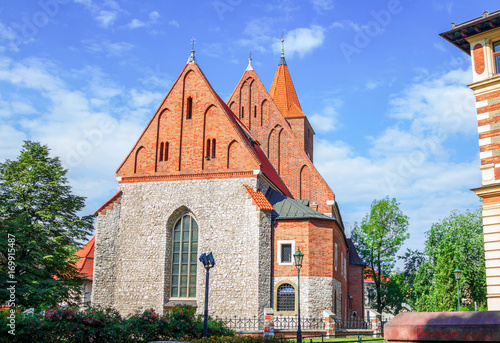 View of old stone Catholic parish building with orange brick roof, arcade window and blooming tea rose bush on a sunny summer day, Poland, Krakow