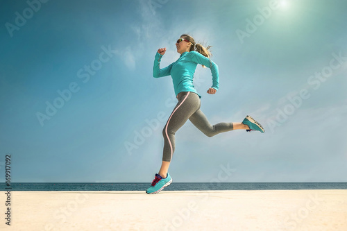 Woman running along the sealine coast under sunlight at sunny su