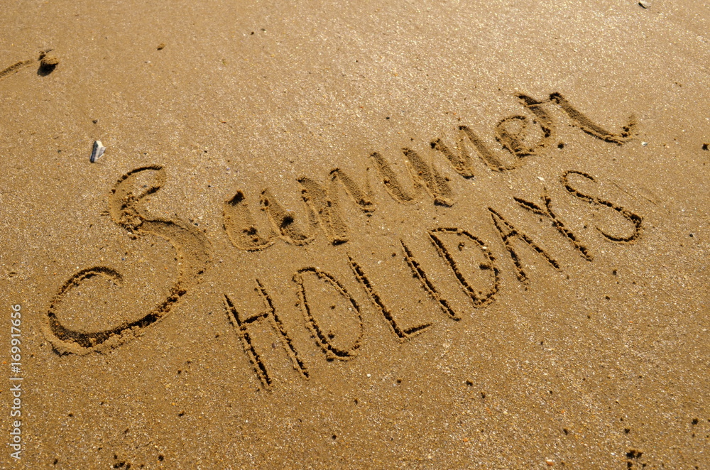 Fototapeta premium SUMMER HOLIDAYS hand lettered in sand on beach with shells