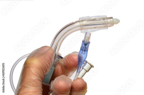 Tracheostomy cannula with white obturator and deflated cuff held in left hand of a doctor in latex sterile glove, white background photo