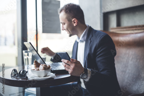Young, modern and positive business man sitting in cafe and doing his job on notebook, cellphone and tablet.