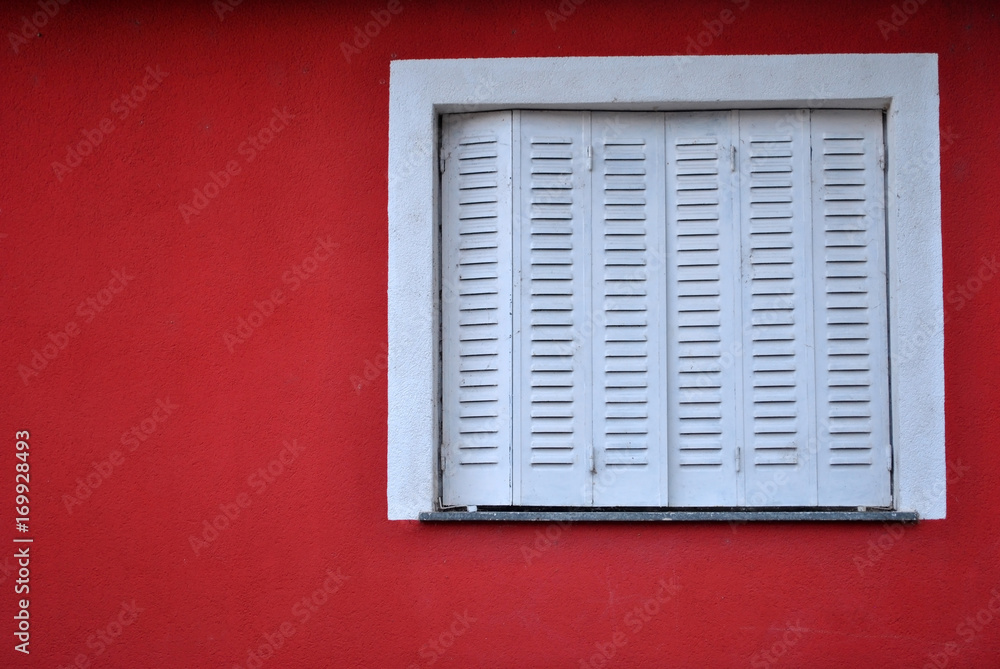 Closed white window on a red colored facade.