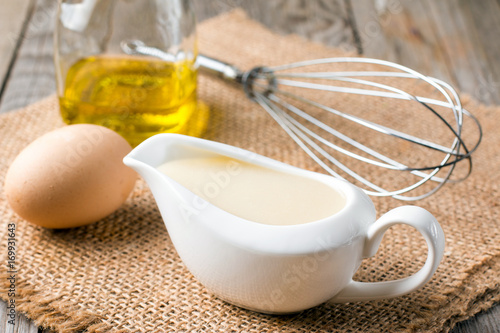 Fresh homemade white sauce Mayonnaise and ingredients eggs, lemon olive oil on wooden background