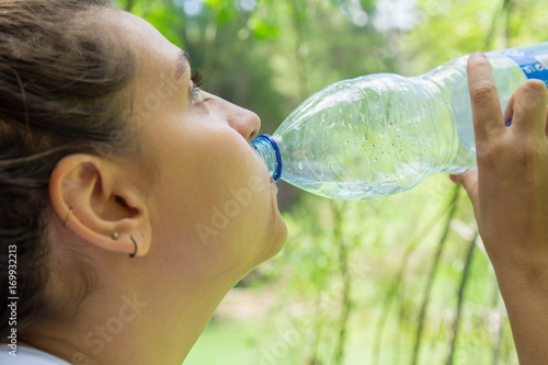 Close-up young woman having water from plastic bottle in the forest.  