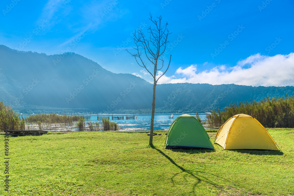 Camping point , The Camping Tent on green grass near river and mountain  with sunlight morning in the summer. Recreation and outdoor travel concept