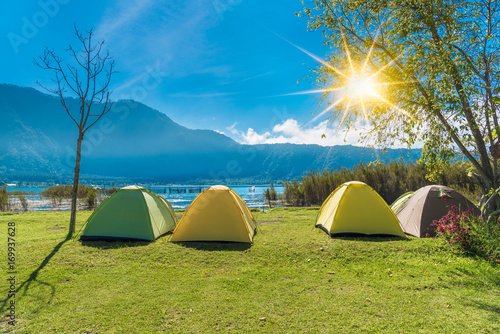 Camping point , The Camping Tent on green grass near river and mountain with sunlight morning in the summer. Recreation and outdoor travel concept