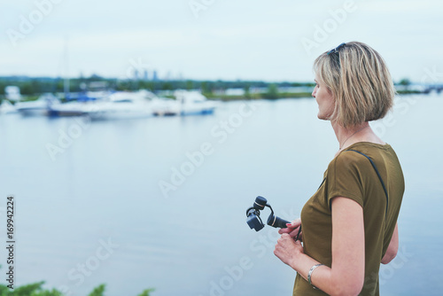 Woman enjoying view in a park, holding small personal camera in hands