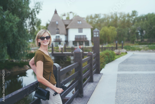 Happy woman in a park, holding small personal camera in hands