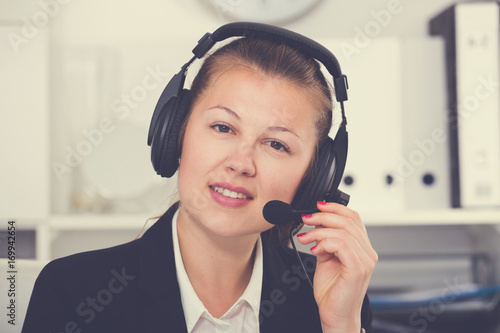 Portrait of young dispatcher female in black suit which is talking by headset with client