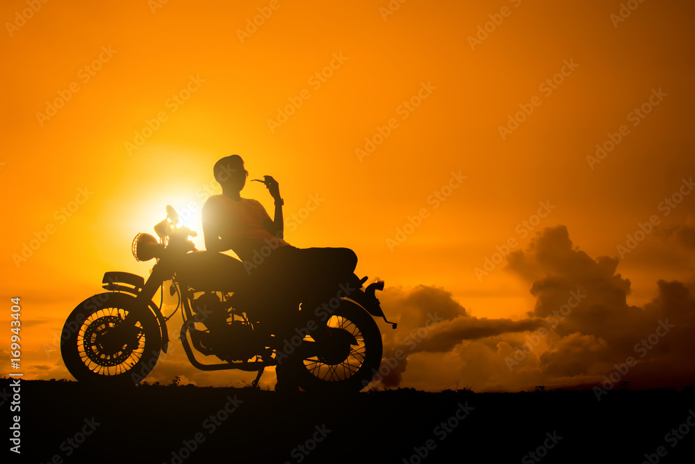 Fototapeta premium Silhouette of biker man sitting smokes with his motorbike beside the natural lake and beautiful, enjoying freedom and active lifestyle, having fun on a bikers tour.sunset background and sky.