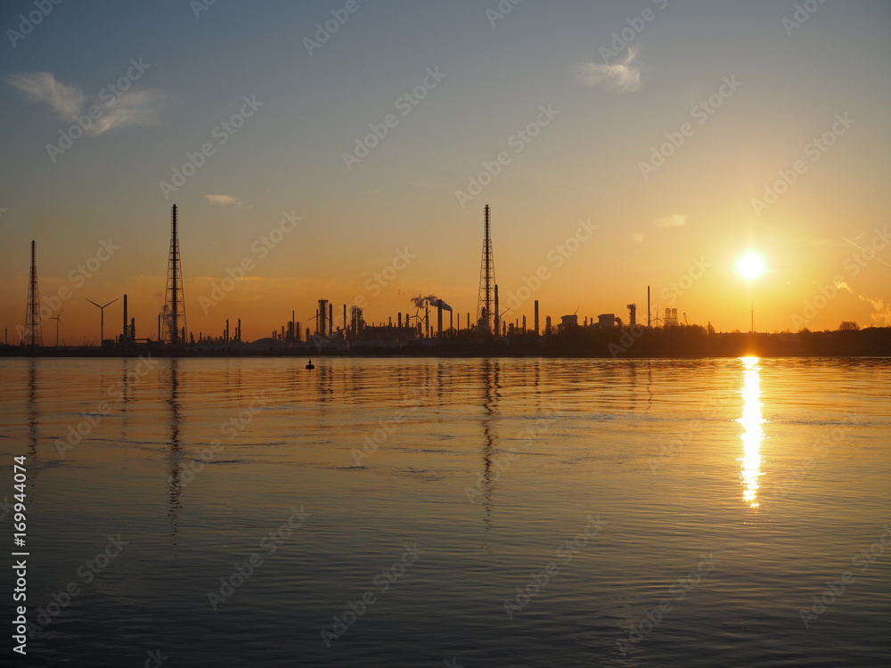 The silhouette of an oiil refinery near the water during sunrise. The silhouette of an oiil refinery near the water during sunrise.