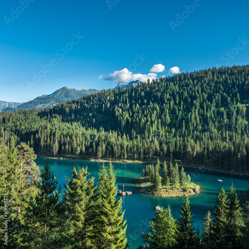 Turqoise mountain lake with a small island encircled by a green coniferous forest in Switzerland
