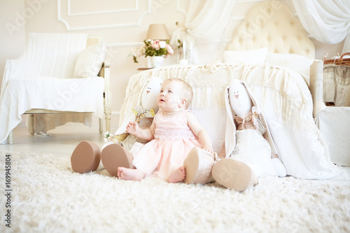 little sad girl sitting between toy rabbits near bed