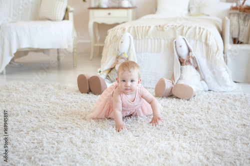little happy girl in pink dress crawling and two toy rabbits behind her