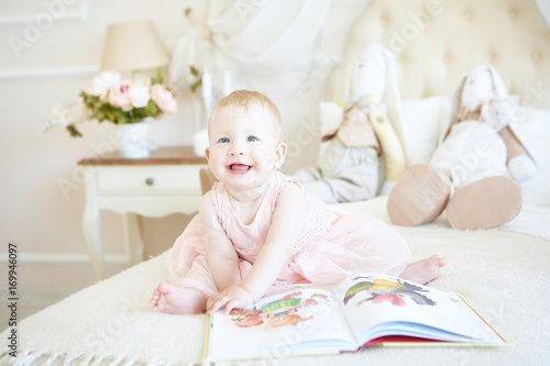 laughing little baby girl flipping a book on the bed